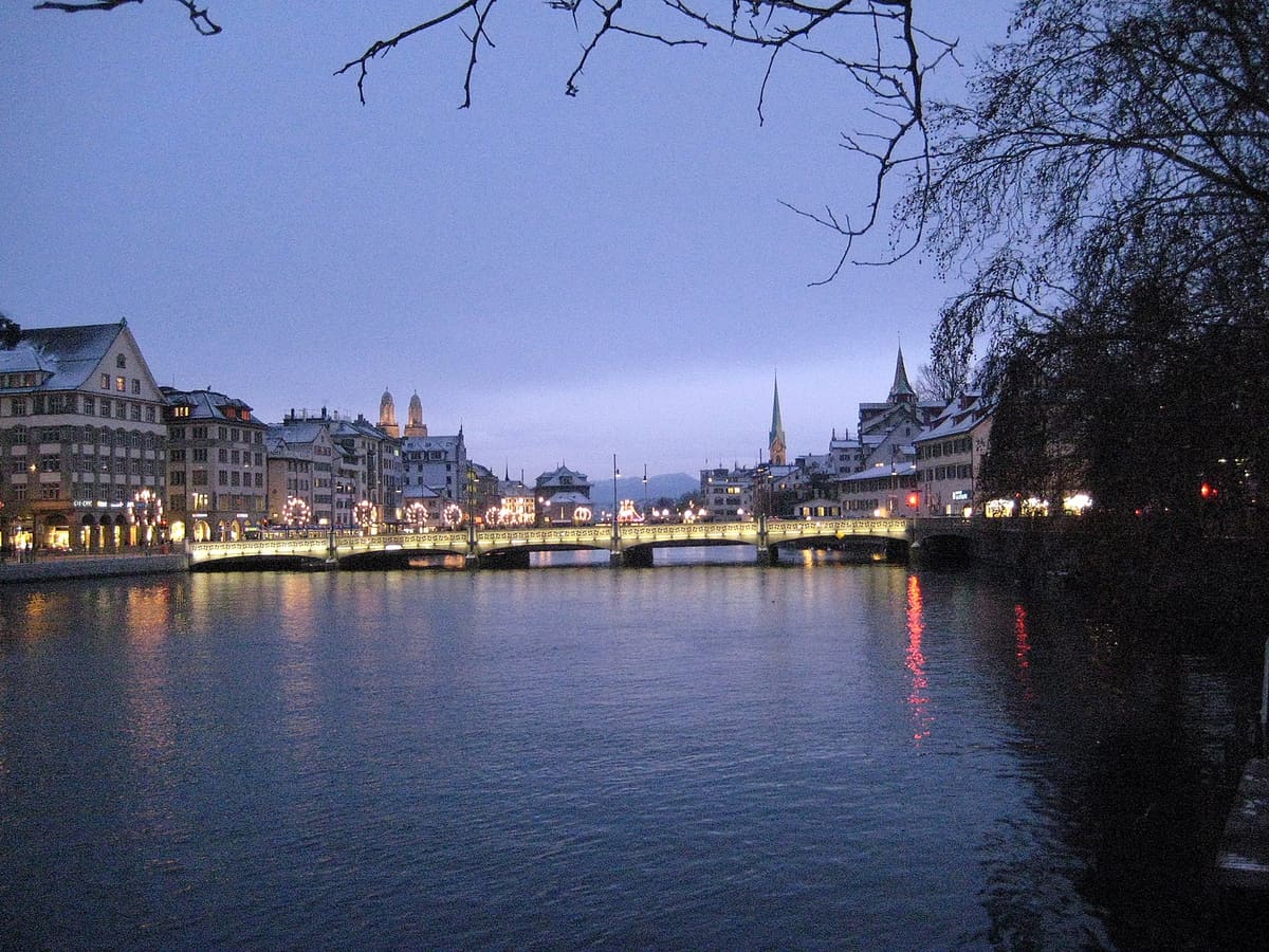 The river Limmat in Zurich at dusk in December with the Rudolf-Brun-Brücke and Christmas lights along the bank